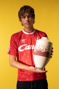 a young man holding up a vase on a yellow background