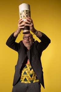 a man holding up a cup on a yellow background